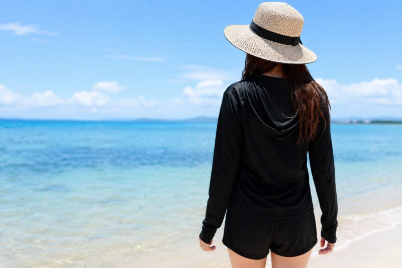 黒いラッシュガードを着た女性が夏の海辺に立つ後ろ姿