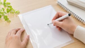 クリアファイルをホワイトボード代わりに使ってペンで書く手元の様子