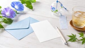 暑中見舞いの例文に合う白いカードと青い封筒、朝顔と風鈴を並べた夏らしい写真
